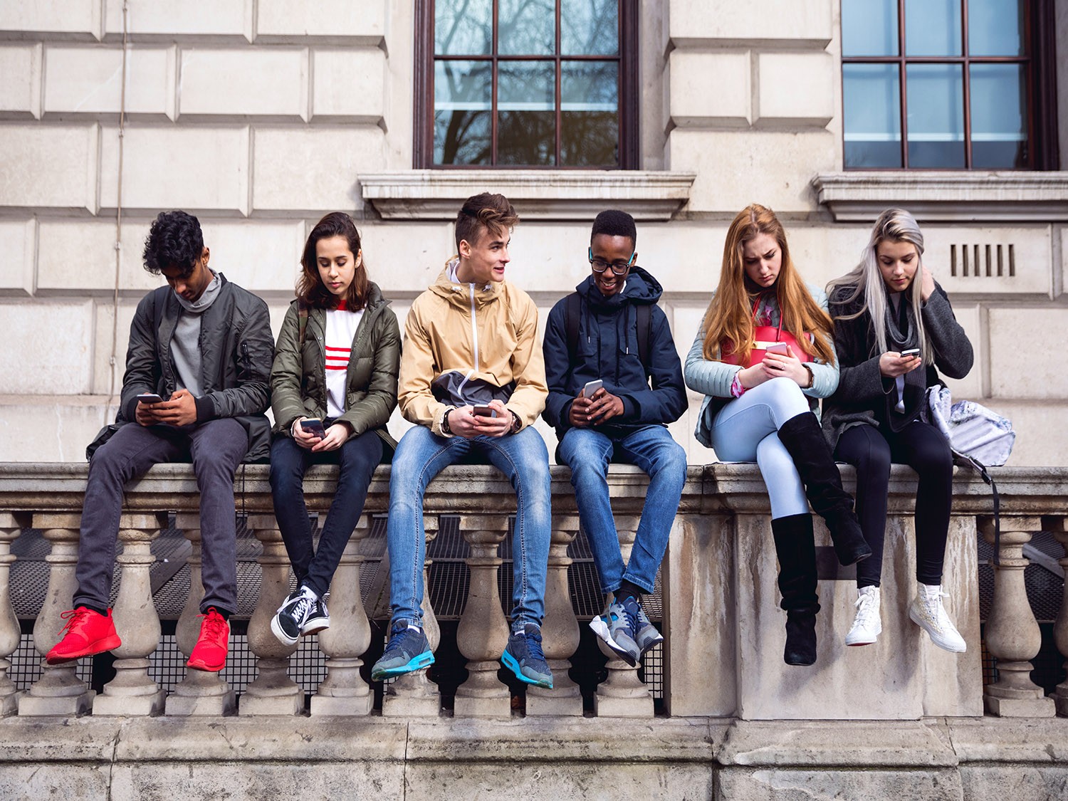 Students sitting on stone wall outside of university building