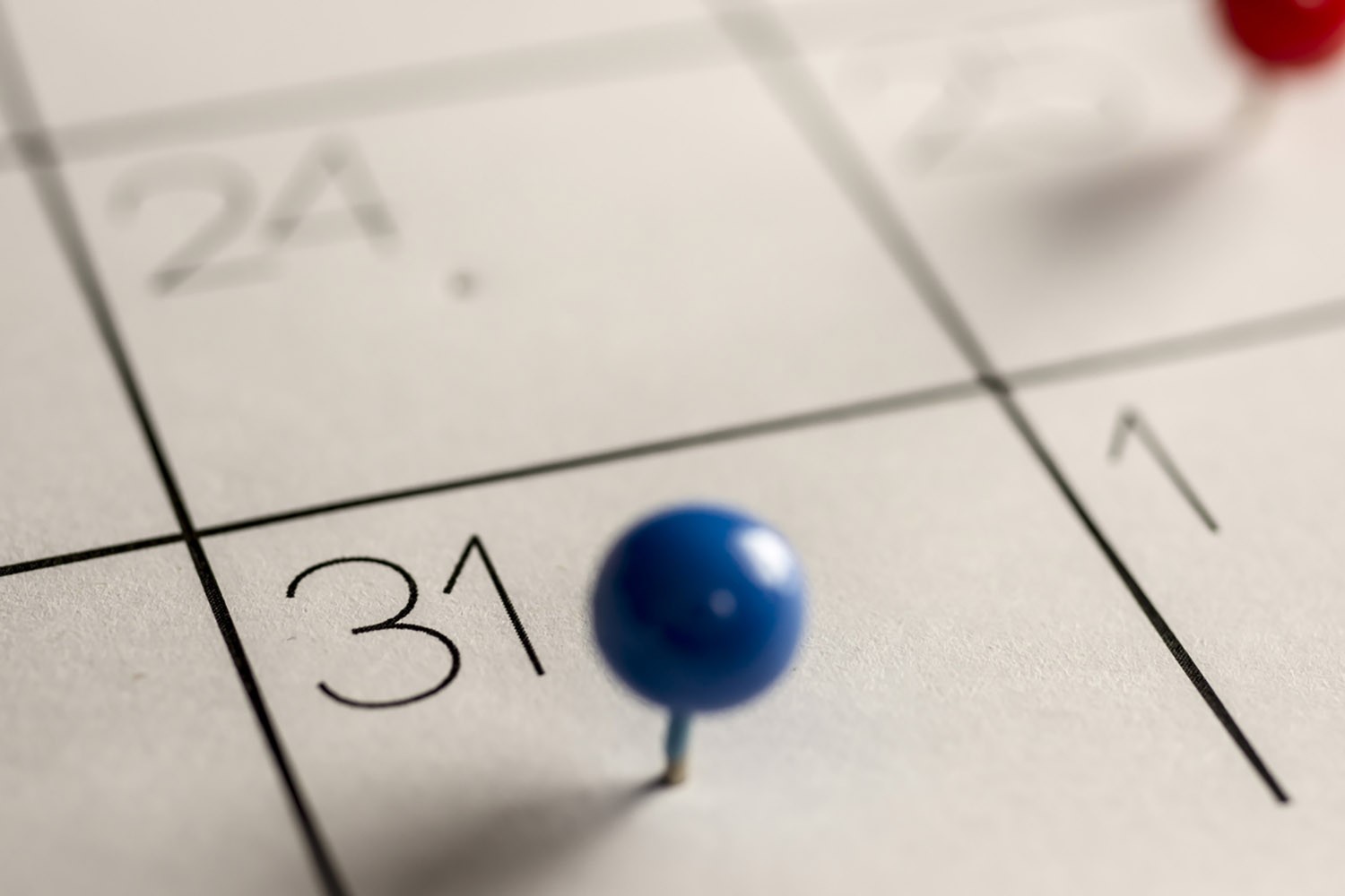 Closeup image of a calendar with a blue pin stuck in the box for the 31st.
